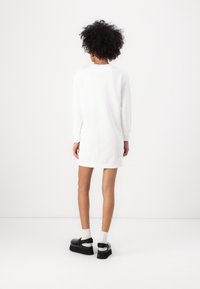 Weißes Sweatshirtkleid mit langen Ärmeln, lockerem Schnitt, gerippten Bündchen und Saum. Dazu schwarze Plateauschuhe und weiße Socken getragen.