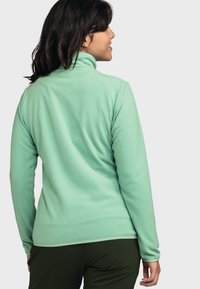 Fleece-Pullover in Hellgrün mit hohem Kragen, langen Ärmeln und glatter Textur, ausgestattet mit einem dezent kurvigen Saum.