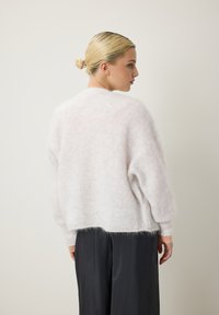 Pull doux et ample de couleur rose clair, fabriqué en matériau pelucheux. Il présente un col rond et des poignets côtelés, avec un ourlet arrière légèrement plus long.