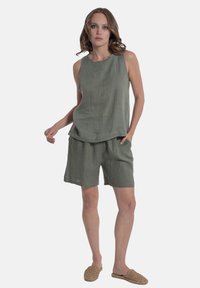Set di top senza maniche e pantaloni shorts in lino di un verde tenue, caratterizzato da una vestibilità rilassata, tasche laterali e una texture leggera. Abbinato a scarpe intramontabili in tessuto.