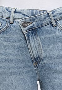 Φωτεινό γαλάζιο τζιν παντελόνι με ορατές θηλιές για ζώνη, μερικώς ανοιχτή μέση και ασημένιο κουμπί με την ένδειξη "Marc O'Polo EST. IN STOCKHOLM."