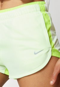 Shorts de sport vert clair avec une texture en mailles, dotés d'un panneau latéral néon vert contrastant et d'un petit logo Nike gris.