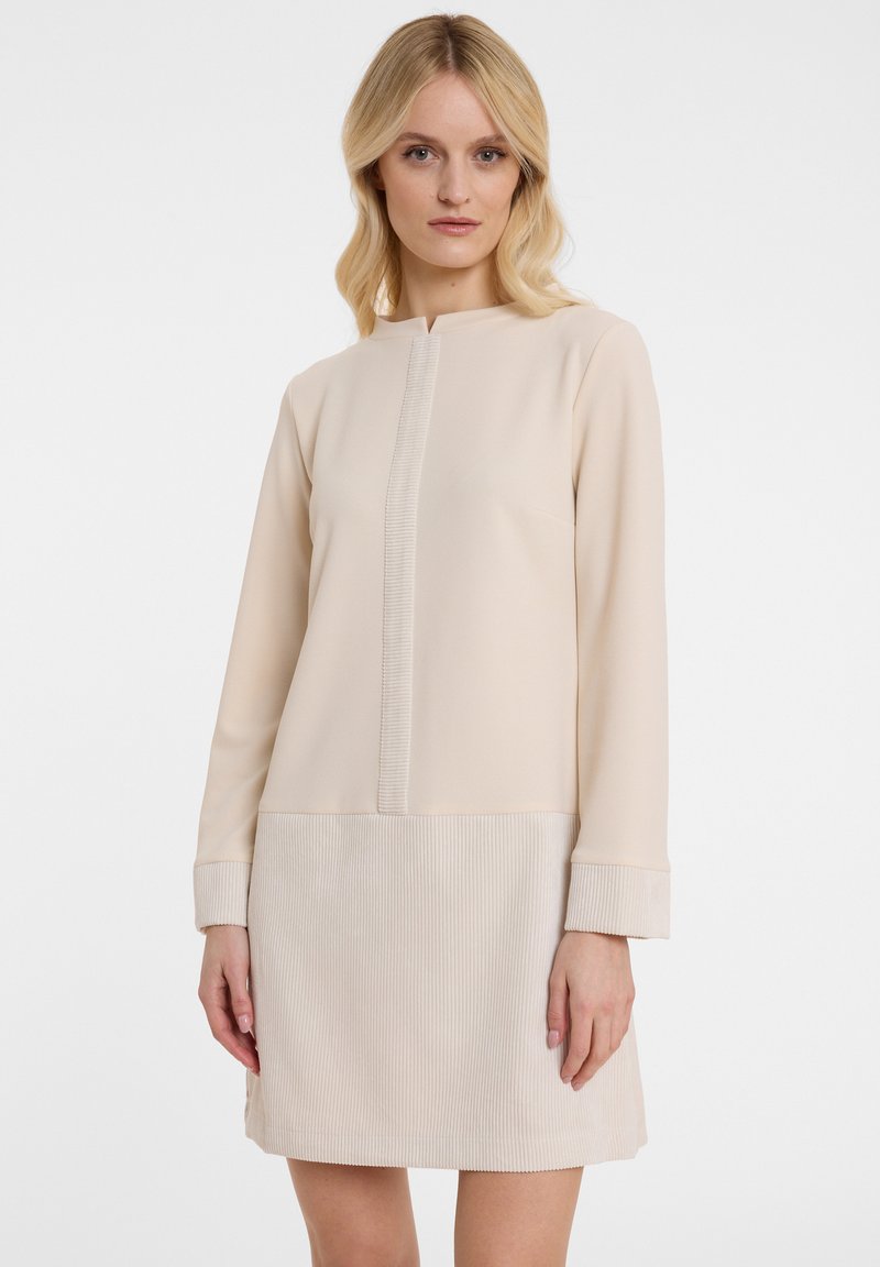 Beiges Shiftkleid mit hohem Kragen, langen Ärmeln, strukturierten Rippakzenten und einem glatten oberen Abschnitt mit einer mittigen Naht.