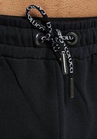 Schwarze Jogginghose mit einem strukturierten Bund, der einen Kordelzug mit metallischen Enden und einem bedruckten Logo hat. Der Stoff ist weich und dehnbar.