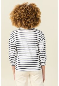 Gestreiftes Langarmoberteil in Weiß und Marineblau, mit einem lockeren Schnitt, Rundhalsausschnitt und gerafften Ärmeln. Der Stoff wirkt weich und texturiert.