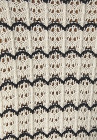 Tessuto lavorato all'uncinetto con intricati motivi a scallop in fili avorio e neri, caratterizzato da una superficie strutturata e un design a trama aperta.