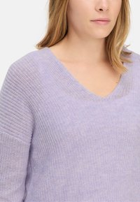 Helllila gestrickter Pullover mit V-Ausschnitt, strukturiertem Stoff und lockeren Ärmeln, der ein entspanntes Design mit einer weichen, luftigen Erscheinung betont.