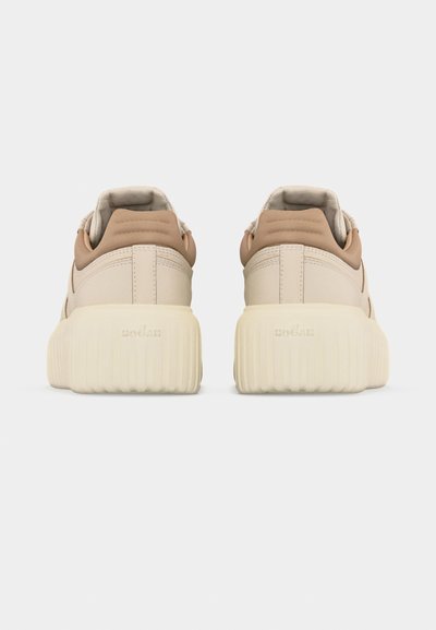 Ζευγάρι μπεζ αθλητικών παπουτσιών με παχιά ριγωτή κρέμ σόλα, επένδυση στον γιακά σε ανοιχτό καφέ, εμφανιζόμενα από πίσω σε λευκό φόντο.