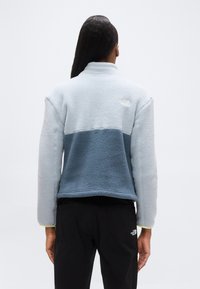 Φλις μπουφάν σε ανοιχτό και σκούρο μπλε, με γιακά με μισό φερμουάρ, υφή υφάσματος και λογότυπο στην άνω πλάτη. Μαύρο παντελόνι.