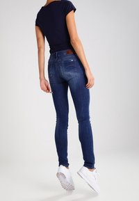 Smaljeans i mörkblått, med medelhög midja och bakfickor, parat med en åtsittande marinblå t-shirt och vita sneakers.