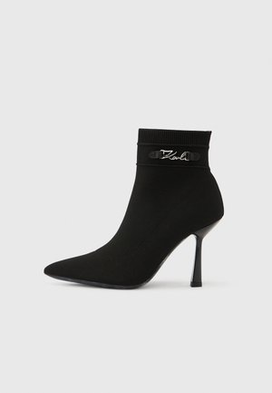 Bota de tornozelo em tecido de malha preto, com biqueira pontiaguda, salto alto fino e detalhe em logo prateado "Karl" perto da aba.