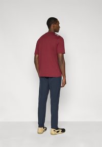 Μπορντό τοπ με κοντά μανίκια και διακριτικές λεπτομέρειες στους ώμους, συνδυασμένο με μπλε σκούρο παντελόνι και μαύρα παπούτσια με μπεζ σόλα. Λεπτή υφή υφάσματος.