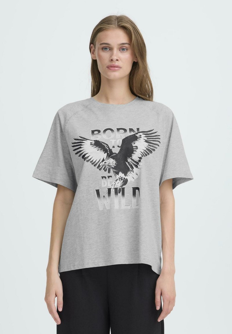 Camiseta gris de gran tamaño hecha de algodón con un estampado gráfico de un águila y el texto "NACIDO PARA SER SALVAJE". Presenta mangas cortas y un corte relajado.