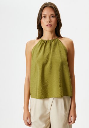 Top sin mangas de color verde oliva con un escote fruncido y un ajuste suelto y texturizado. Combinado con pantalones beige claros a medida.