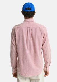 Rood-wit gestreepte langärmige shirt met een button-down kraag, voorzien van een rugplooi en afgeronde zoom, gecombineerd met een blauwe pet.