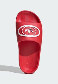 Raudonas atviras sandalai iš sintetinio audinio. Ant dirželio yra baltas logotipas, tekstūruotas vidinis padas ir lygus išorinis paviršius.