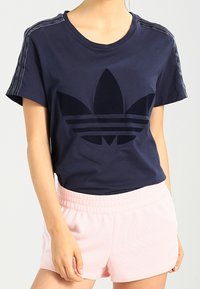 Marineblauwe katoenen t-shirt met een groot zwart Adidas-logo op de voorkant. Heeft gestikte strepen op de mouwen en een ronde halslijn.