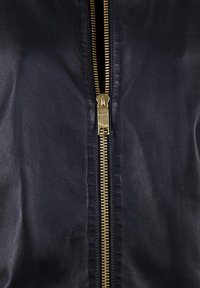 Marineblå læderjakke med en fremtrædende gylden lynlås, glat tekstur og minimalistisk design uden ekstra accenter eller mønstre.