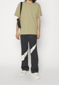 Kaki bomulls t-shirt med logotyp, svarta nylonbyxor med vita diagonala accenter, tillsammans med grå sneakers. Enkelt design, avslappnad passform.