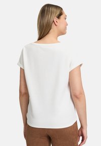 Biała bluzka z krótkim rękawem i okrągłym dekoltem oraz podwiniętymi rękawami. Wykonana z teksturowanej tkaniny, charakteryzuje się luźnym krojem i zaokrąglonym dołem.