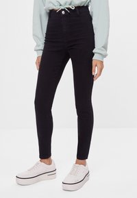 Svarta högmidjade skinny jeans i denim, med knappstängning fram, kontrasterande sömmar och en smal, figurnära silhuett.