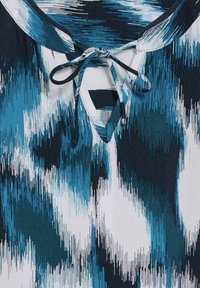 Maglietta a maniche corte con un motivo astratto in tonalità teal e navy, scollatura a V e dettaglio di cravatta al colletto, realizzata in un tessuto leggero.