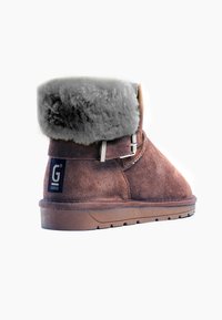 Stivale alla caviglia in suede marrone con risvolto in pelliccia grigia, dettaglio in fibbia argentata e suola in gomma. Presenta cuciture decorative e logo sul lato.