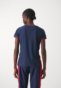 Top atlético azul marino de mangas cortas, con ribetes rojos en las mangas y los lados. Tejido suave y ligero con un corte relajado.