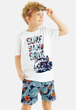 White T-shirt with colorful "SURF SAND SOUL" text and van graphic; paired with navy shorts featuring tropical floral patterns in orange and teal.
