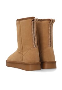 Wysokie beżowe zamszowe botki o gładkiej fakturze, z bocznym zamkiem i kontrastującymi przeszyciami. Podeszwa zewnętrzna jest brązowa i teksturowana, zapewniając dobrą przyczepność.