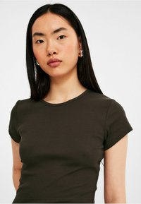 T-shirt côtelé vert olive foncé avec un col rond et des manches courtes, présentant un design ajusté et une texture lisse.