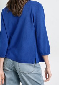 Blå stickad tröja med trekvartslånga ärmar, ribbat nederkant och sidofickor, som är ihop med ljusblå jeans. Mjuk textur, avslappnad passform.