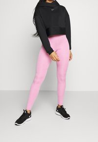 Černá krátká mikina s logem, spárovaná s růžovými legínami. Outfit doplněný černými sportovními botami, což podtrhuje sportovní vzhled.