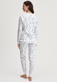 Witte pyjama-set met een winterthema, versierd met kleine prints van sneeuwpoppen en bomen. Gemaakt van zachte stof en voorzien van geribde manchetten aan de broek en mouwen.