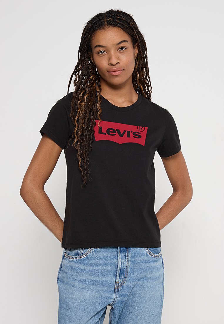 Czarna bawełniana koszulka z okrągłym dekoltem i krótkimi rękawami, z czerwonym logo Levi's na przodzie. W zestawie z jasnoniebieskimi dżinsami.