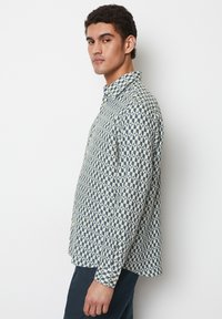 Hemd mit Knopfleiste in einem geometrischen Blau- und Crememuster, mit umklappbarem Kragen, langen Ärmeln und geradem Saum. Der Stoff hat eine glatte Textur.