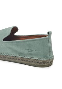 Scarpa slip-on in suede verde con design arrotondato, suola in juta beige cucita e interno in pelle liscia. "COLLEZIONE FRED MARTIN" impressa.