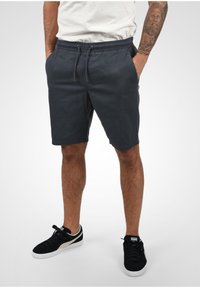Shorts navy en tissu mélangé de coton, dotés d'une taille élastique, d'une fermeture à cordon et de poches latérales. Modèle portant des baskets noires.