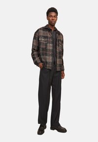 Schwarze, rote und graue karierte Jacke aus einem entspannten Stoff, mit entspannter Passform, Knopfverschluss und zwei Brusttaschen, kombiniert mit schwarzen Hosen und Schuhen.