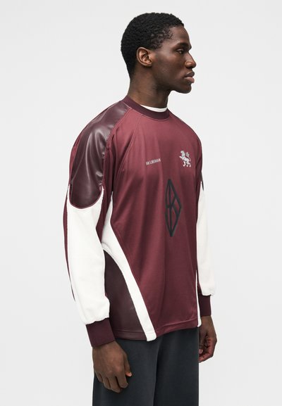 Burgundia värvi pusa valgete fliiskattete, pikkade varrukate, logotrüki ja geomeetrilise mustriga. Sile tekstuur ja soonilised mansetid.