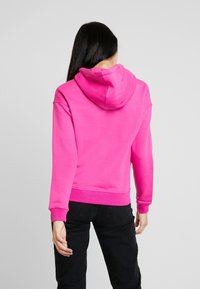 Mikina s kapucí v jasně růžové barvě, vyrobená z měkké tkaniny s elastickými manžetami a lemem, s uvolněným střihem a minimálním designem.