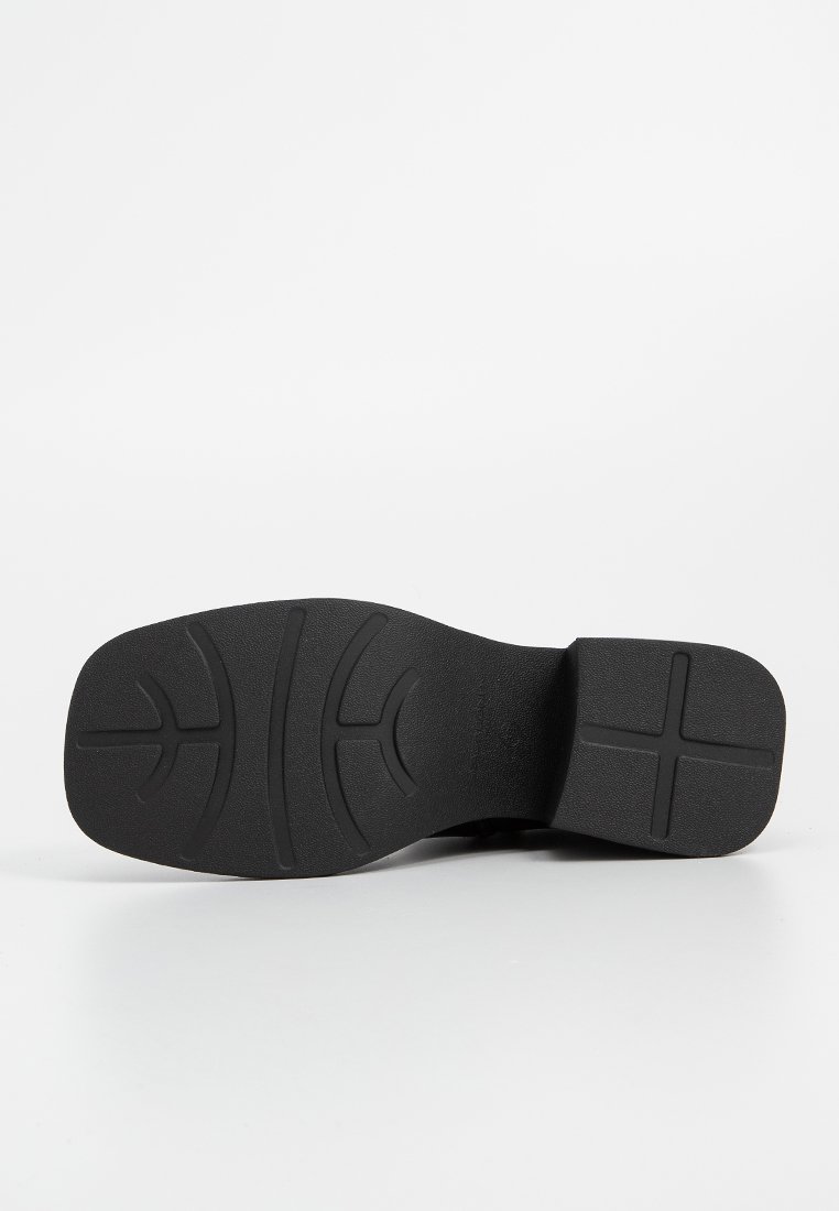 Zwarte rubberen schoenzool met een patroon in de loop, met een platte hak en een ronde neus. Gelaagde oppervlakte voor grip en stabiliteit.