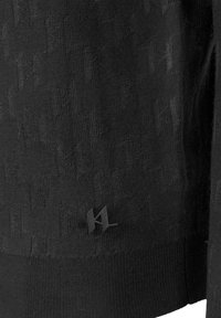 Czarna dzianina z delikatnym wzorem splecionych kształtów. Na dole znajduje się mały czarny akcent w postaci logo.