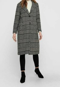 Schwarz-weißer Hahnentopp-Muster Mantel; langes Design mit Knopfleiste und breitem Revers; kombiniert mit schwarzen Leggings und Ankle Boots.