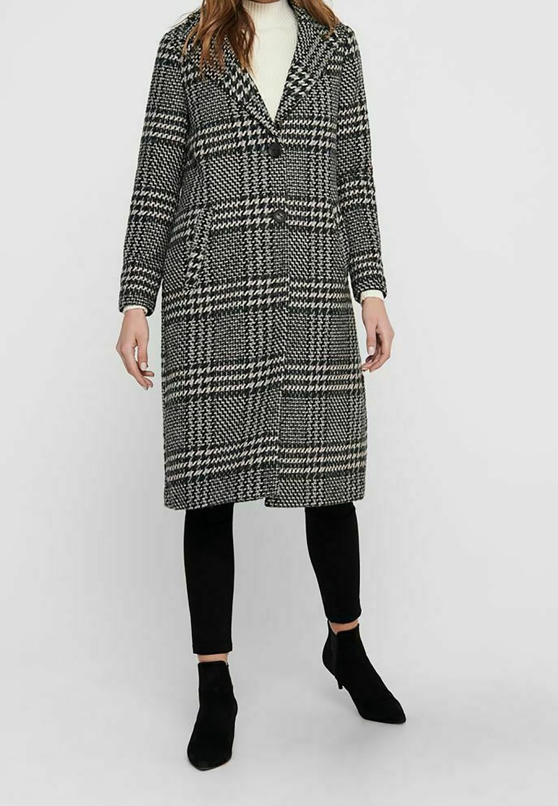 Schwarz-weißer Hahnentopp-Muster Mantel; langes Design mit Knopfleiste und breitem Revers; kombiniert mit schwarzen Leggings und Ankle Boots.