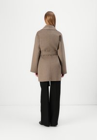Brun ullblanding frakk med belte i livet, vide ermer og krage med spiss. Slim fit, kombinert med svarte vide bukser.