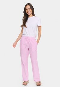 Pink and white striped pants with a drawstring waist, made of a lightweight fabric, paired with a plain white t-shirt and light-colored sandals.