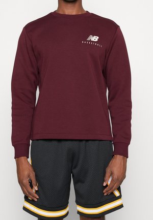 Felpa bordeaux a manica lunga con colletto rotondo e logo bianco "New Balance Basketball" sul petto, abbinata a pantaloni corti in rete neri con strisce gialle.