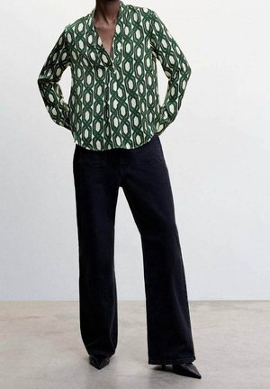 Green and white patterned blouse with a loose fit and a deep V-neck. Paired with high-waisted, black wide-leg pants and pointed-toe heels.