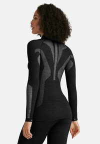 Haut de sport noir à manches longues avec un motif texturé gris à l'arrière, fabriqué en tissu extensible, avec un design ajusté et des ouvertures pour les pouces.
